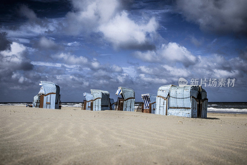 蓝色的沙滩椅子在Egmont aan Zee的北海海岸，荷兰在一个戏剧性的天空下